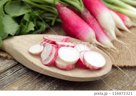 Fresh ripe vegetables on the wooden table with burlap table cloth - radish sliced on a big spoon and whole ones, green onion are ready to cook salad. Fresh ripe vegetables on the wooden table with burlap table cloth - radish sliced on a big spoon and whole ones, green onion are ready to cook salad. 116872321