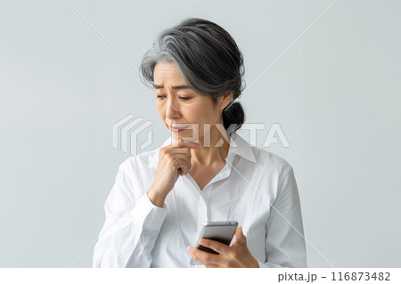 悩みながらスマートフォンを操作するシニアのアジア人女性（下を向く） 116873482