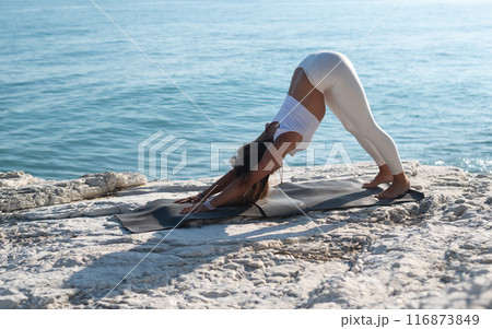 A woman in white sports clothes practices yoga exercises outdoors among white cliffs overlooking the sea A woman in white sports clothes practices yoga exercises outdoors among white cliffs overlooking the sea 116873849