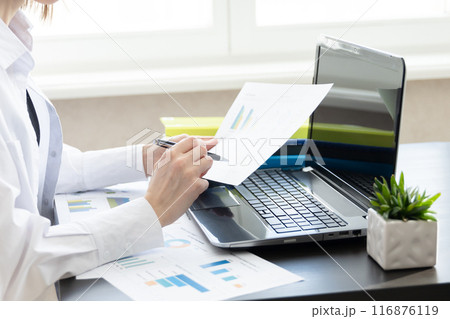 Business woman holding paper account documents, working at the table at the workplace with a laptop computer in the office indoors. The concept of working with financial documents 116876119