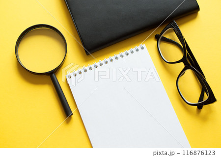 Business concept with notebook, magnifier and black glasses on yellow background for your design Business concept with notebook, magnifier and black glasses on yellow background for your design 116876123