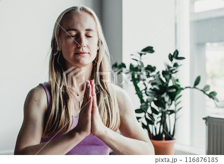 Young attractive woman practicing yoga, sitting in Padmasana, exercise, Lotus pose, namaste, working out, wearing sportswear, near floor window Young attractive woman practicing yoga, sitting in Padmasana, exercise, Lotus pose, namaste, working out, wearing sportswear, near floor window 116876185