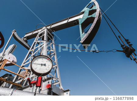 Oil pump jack operating under clear blue sky at oil field during daytime work hours 116877898