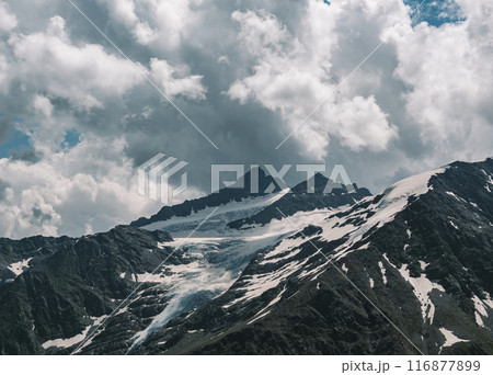 Stunning snow-covered mountain peaks under dramatic cloudy sky during daytime hiking adventure 116877899