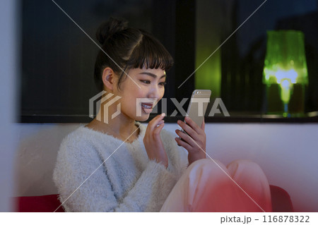 スマートフォンを操作する笑顔の若い女性 夜の自宅 イメージ スマートフォンを操作する笑顔の若い女性 夜の自宅 イメージ 116878322