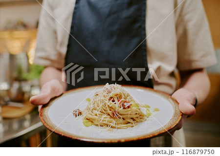 Medium close up of ceramic round plate with spaghetti carbonara covered with parmigiano, unrecognizable male hand holding plate Medium close up of ceramic round plate with spaghetti carbonara covered with parmigiano, unrecognizable male hand holding plate 116879750