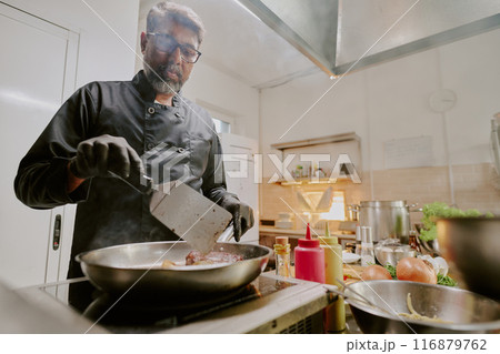 Low angle shot of Indian chef cooking steak in modern kitchen of popular restaurant Low angle shot of Indian chef cooking steak in modern kitchen of popular restaurant 116879762