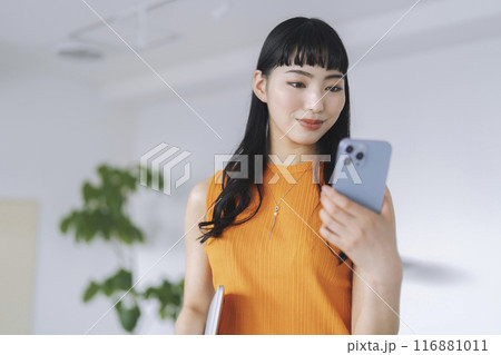 オフィスでスマートフォンの画面を見る若いビジネスウーマン 116881011