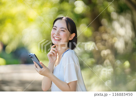 日差しの中でスマホを見る若い女性 116883450