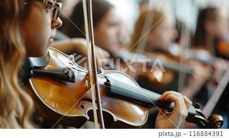 a close-up of a young violinist playing with a group of musicians, focusing on the instrument  116884391