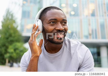 Music song concept. Good start day. Happy African American man listening modern hit on street in city. Person guy wearing headphones enjoy listening favorite music outdoor. People lifestyle joy Music song concept. Good start day. Happy African American man listening modern hit on street in city. Person guy wearing headphones enjoy listening favorite music outdoor. People lifestyle joy 116886941
