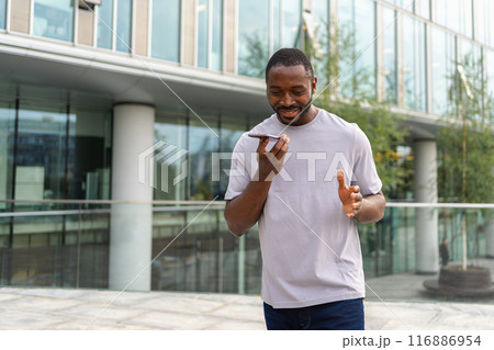 African american man talking on smartphone on street in city outdoor. Man with cell phone chatting with friends. Smiling person making answering call by cellphone. Guy having conversation by mobile 116886954