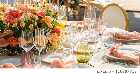 Wedding banquet concept. Chairs and round table for guests, served with cutler and, flowers and crockery and covered with a tablecloth Wedding banquet concept. Chairs and round table for guests, served with cutler and, flowers and crockery and covered with a tablecloth 116887715