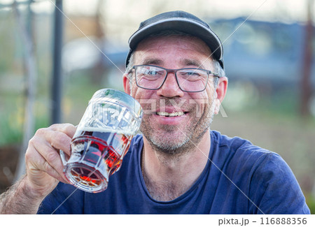 a man is surprised while taking a large glass of beer to his mouth and is very happy to cool off from it. Beer is a drink that is preferred by boys and preferred during the summer. 116888356