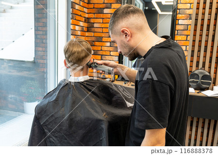 Picture of a milling process in a barbershop studio, a blond boy with blue eyes and freckles is very happy and will have a new style of milling. Picture of a milling process in a barbershop studio, a blond boy with blue eyes and freckles is very happy and will have a new style of milling. 116888378