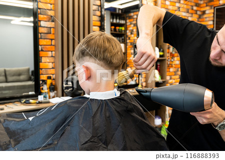 Master Barber hairstyle and styling with dryer hair to guy. Concept Barbershop. Soft focus. Master Barber hairstyle and styling with dryer hair to guy. Concept Barbershop. Soft focus. 116888393