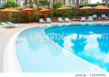 Step into a luxurious pool with a strip of coastal sand and brightly colored umbrellas and sun loungers 116888902