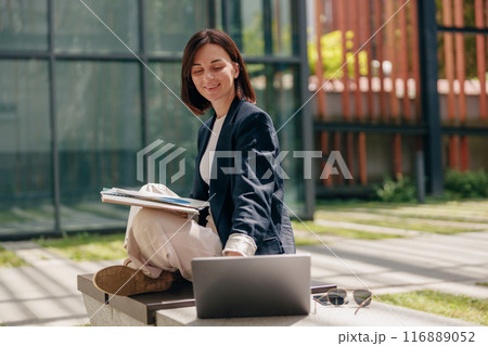 Smiling Female Professional Working Outdoors with Laptop, Clipboard and Sunglasses 116889052