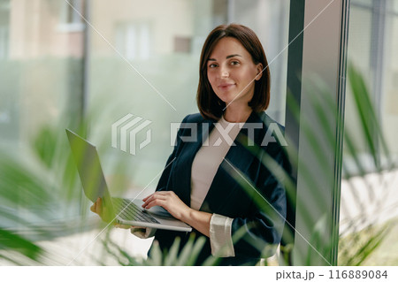 Confident and ambitious businesswoman focused on laptop work in a modern office setting Confident and ambitious businesswoman focused on laptop work in a modern office setting 116889084