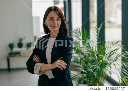 A confident, successful woman is standing in a sleek, contemporary office space 116889097