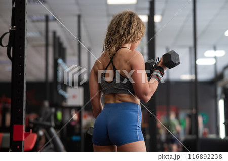 Muscular Caucasian forty year old woman doing exercises with dumbbells in the gym.  116892238