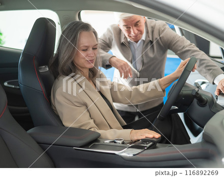 An elderly couple chooses a new car at a car dealership. Mature woman driving.  116892269