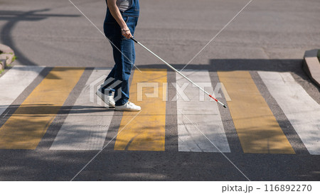 Close-up of the legs of a blind woman crossing the road at a crosswalk with a cane.  116892270