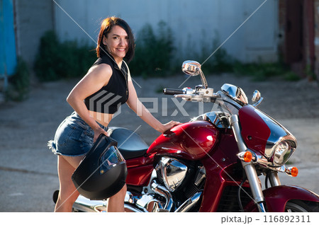 Brunette woman looks in the rearview mirror on a motorcycle. Brunette woman looks in the rearview mirror on a motorcycle. 116892311