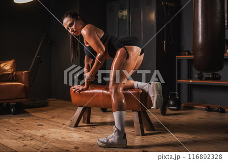 Caucasian woman doing one arm dumbbell row on a bench in a retro gym. Caucasian woman doing one arm dumbbell row on a bench in a retro gym. 116892328