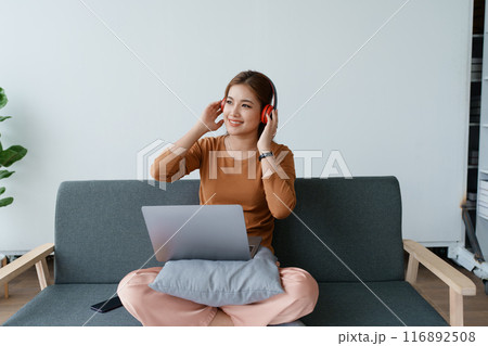 A woman feels utterly relaxed as she sits with her headphones, listening to music on her laptop A woman feels utterly relaxed as she sits with her headphones, listening to music on her laptop 116892508