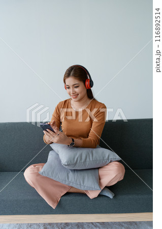 A woman feels utterly relaxed as she sits with her headphones, listening to music on her smartphone 116892514