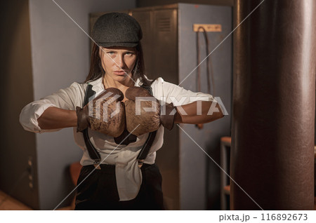 A woman posing with boxing gloves. Retro style Peaky Blinders.  116892673