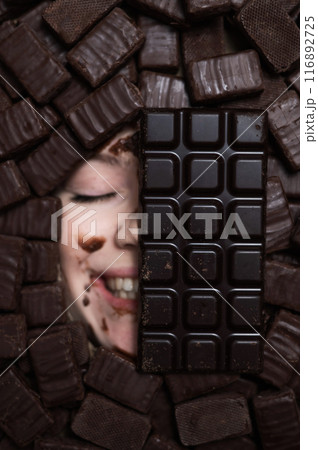 The face of a caucasian woman surrounded by sweets. The girl is smeared in chocolate. The face of a caucasian woman surrounded by sweets. The girl is smeared in chocolate. 116892725