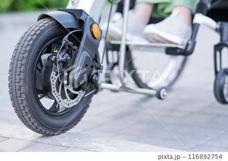 A faceless woman in a wheelchair with an assistive device for manual control. Electric handbike.  116892754