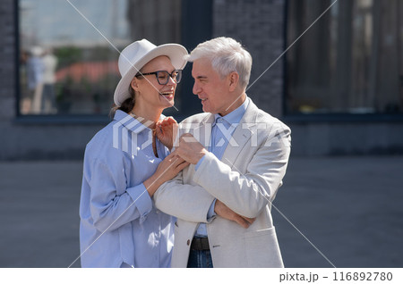 An elderly couple in love walks through the city. Portrait of a stylish gray-haired man and woman.  116892780