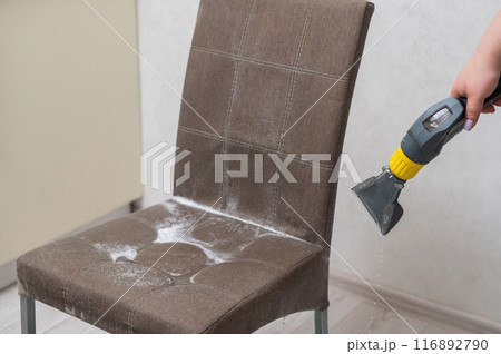 Woman cleaning a fabric chair with a professional washing vacuum cleaner.  116892790