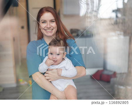 View through the window of a red-haired Caucasian woman holding her little son.  116892805