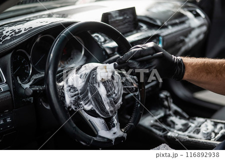 A mechanic cleans the interior of a car with a brush and foam. A mechanic cleans the interior of a car with a brush and foam. 116892938