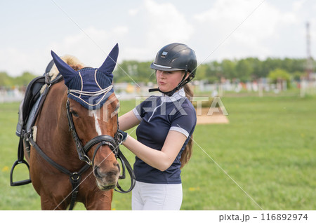 A young girl stands next to a horse before an equestrian competition. A young girl stands next to a horse before an equestrian competition. 116892974