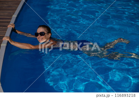 An elderly woman in sunglasses swims in the pool. Vacation in retirement.  116893218