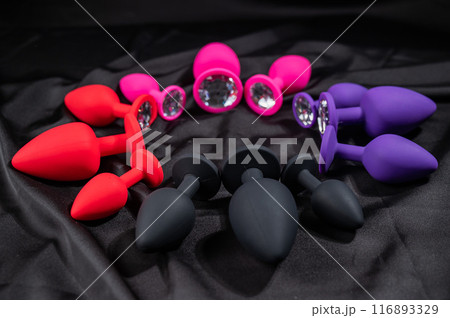 A set of silicone anal plugs in different colors and sizes on a black silk sheet.  116893329