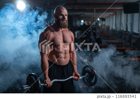 Caucasian bald topless man doing an exercise with a barbell in the gym. Bicep curls with weights. Caucasian bald topless man doing an exercise with a barbell in the gym. Bicep curls with weights. 116893541