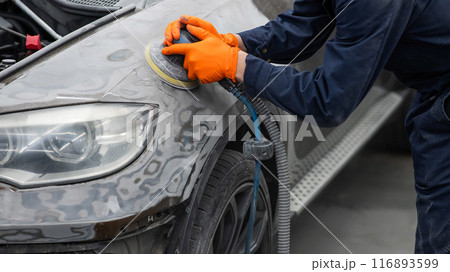 A mechanic sands the putty on a car body with a machine. Repair after an accident.  116893599