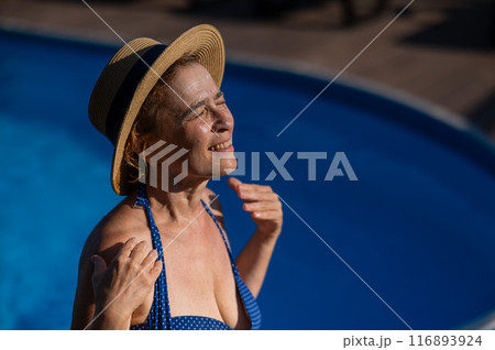Portrait of an older woman applying sunscreen to her face while on vacation. Portrait of an older woman applying sunscreen to her face while on vacation. 116893924