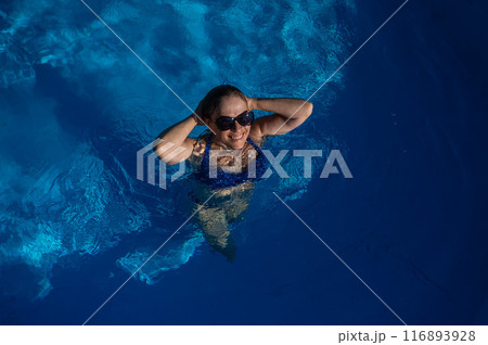 An elderly woman in sunglasses swims in the pool. Vacation in retirement.  116893928