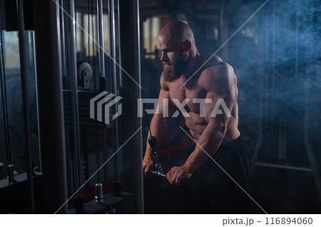 Bald Caucasian Bodybuilder doing heavy triceps exercises with cable.  116894060