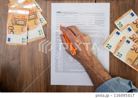 Agricultural worker completes 1040 tax form with pen in hand detailing seasonal earnings and travel expenses to determine tax liability sitting at table with euro bills Agricultural worker completes 1040 tax form with pen in hand detailing seasonal earnings and travel expenses to determine tax liability sitting at table with euro bills 116895817