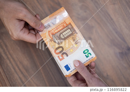 Male company accountant gives euro banknotes to female worker for currency exchange service with favorable rates sitting at wooden table in local bank Male company accountant gives euro banknotes to female worker for currency exchange service with favorable rates sitting at wooden table in local bank 116895822