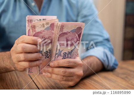 Man counting Turkish lira banknotes at a wooden table. Financial concept depicting economy, inflation, and savings  116895890