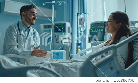 Male doctor talking to a female patient in a hospital bed surrounded by medical equipment. Emphasizing patient care and hospital treatment in a clinical setting. 116896779